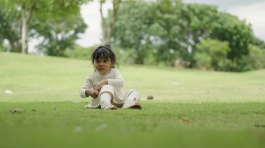 Küçük kız parktaki yeşil çimlerde oturuyor.