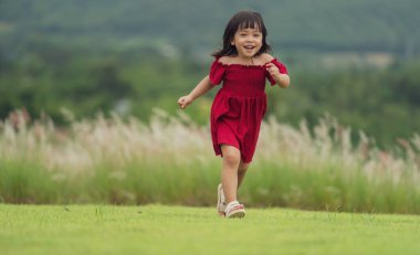 Kırmızı elbiseli mutlu kız çim tarlasında koşuyor.