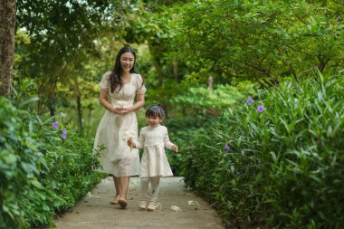 Mutlu anne ve küçük kız çiçek bahçesinde yürüyen beyaz elbiseli