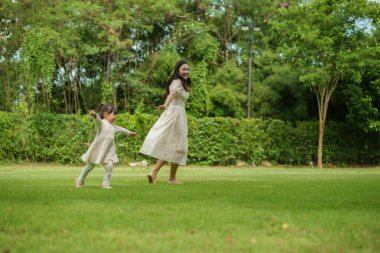 Anne ve küçük kız parkta çim tarlasında koşuşturmaca oynuyorlar.