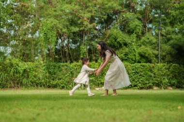 Anne ve küçük kız parkta çimenlik alanda oynuyorlar.