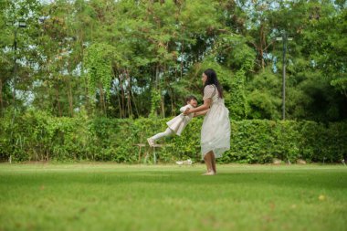 Anne ve küçük kız parkta çim tarlasında oynuyorlar.