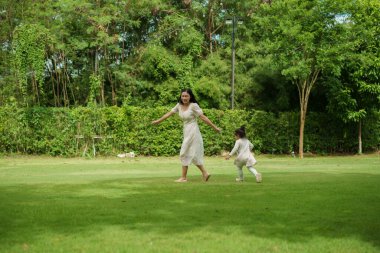 Anne ve küçük kız parkta çim tarlasında koşuşturmaca oynuyorlar.