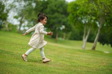 Yeşil çim tarlasında koşan beyaz elbiseli mutlu kız.