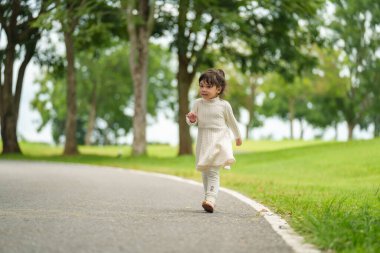 Mutlu küçük kız parkta bir patika boyunca yürüyor.