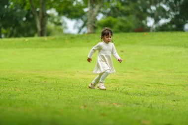 Yeşil çim tarlasında koşan beyaz elbiseli mutlu kız.