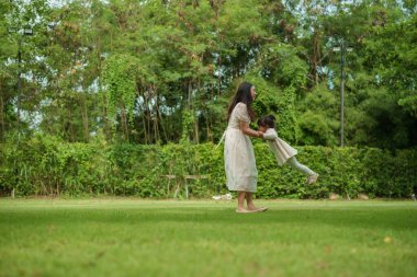 Anne ve küçük kız parkta çim tarlasında oynuyorlar.