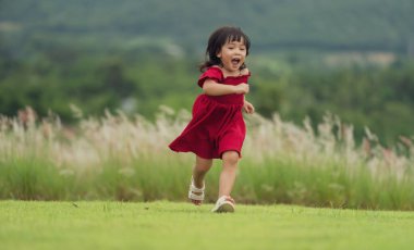 Kırmızı elbiseli mutlu kız çim tarlasında koşuyor.