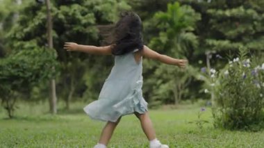 Yavaş çekimde, yeşil çimen tarlasında yürüme oyunu oynayan küçük mutlu kız.