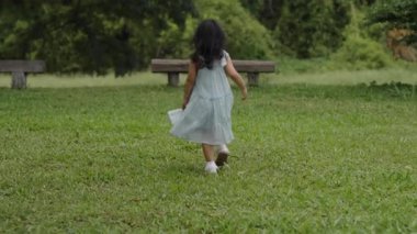 Mavi elbiseli küçük kız yeşil çimlerde yürüyor.