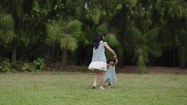 Anne, küçük kızın elini tutarken parkta çim tarlasında yürüme ve koşma oyunu oynuyor.