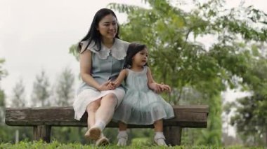 Mutlu anne ve küçük kız ahşap bir bankta oturuyor ve parkta birlikte konuşuyorlar.