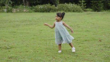 Yeşil çim tarlasında oynayan, yürüyen, giysili mutlu kız.