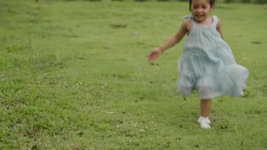 Yeşil çim tarlasında koşan, küçük, mutlu bir kızın yavaş çekimi.