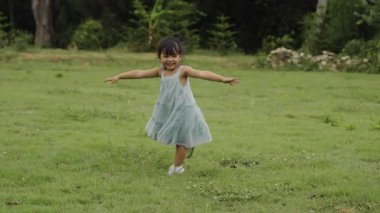 Yavaş çekimde, yeşil çimen tarlasında yürüme oyunu oynayan küçük mutlu kız.