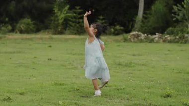 Yeşil çim tarlasında çember çizerek yürüyen, elbiseli mutlu bir kız.