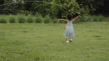 Yeşil çim tarlasında yürüyen küçük mutlu kız.