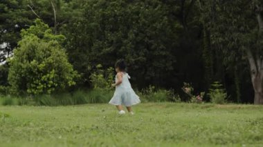 Yeşil çim tarlasında koşan, giysili mutlu bir kız.