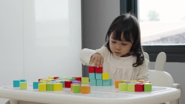 Küçük kız bir masanın üzerine küp inşa etmek için blok oyuncağı oynuyor.