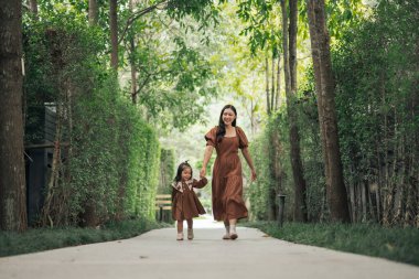 Kahverengi elbiseli mutlu anne ve küçük kız bahçede yürüyor.