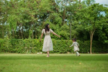 Anne ve küçük kız parkta çim tarlasında koşuşturmaca oynuyorlar.