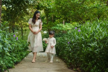 Mutlu anne ve küçük kız çiçek bahçesinde yürüyen beyaz elbiseli