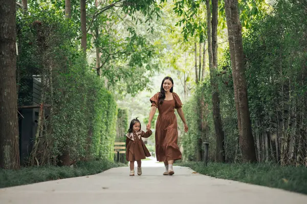 Kahverengi elbiseli mutlu anne ve küçük kız bahçede yürüyor.