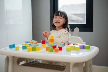 Mutlu küçük kız bir masanın üzerine küp inşa etmek için blok oyuncağı oynuyor.