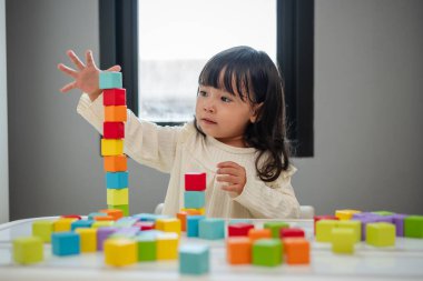 Küçük kız bir masanın üzerine küp inşa etmek için blok oyuncağı oynuyor.
