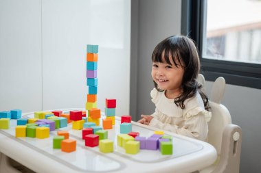 Mutlu küçük kız bir masanın üzerine küp inşa etmek için blok oyuncağı oynuyor.