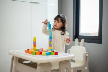 Küçük kız bir masanın üzerine küp inşa etmek için blok oyuncağı oynuyor.