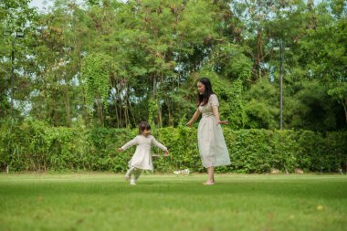 Anne ve küçük kız parkta çim tarlasında koşuşturmaca oynuyorlar.