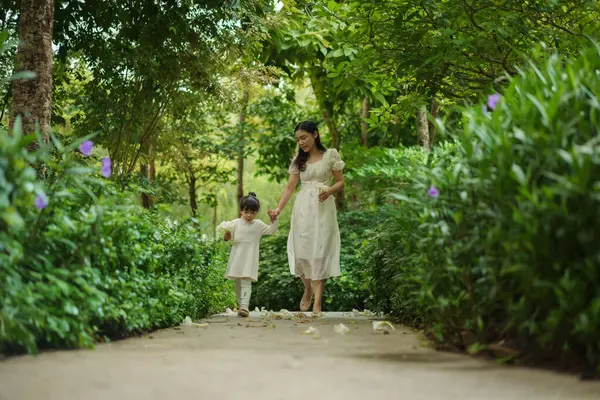 Mutlu anne ve küçük kız çiçek bahçesinde yürüyen beyaz elbiseli