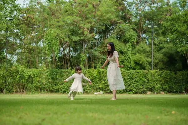 Anne ve küçük kız parkta çim tarlasında koşuşturmaca oynuyorlar.