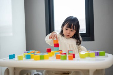 Küçük kız bir masanın üzerine küp inşa etmek için blok oyuncağı oynuyor.