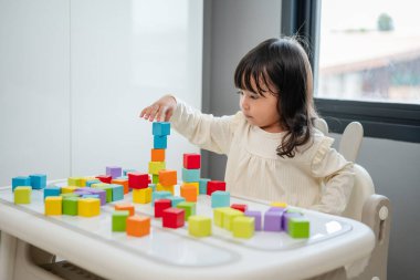 Küçük kız bir masanın üzerine küp inşa etmek için blok oyuncağı oynuyor.