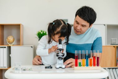 toddler girl scientist looking through a microscope. learning science with her father