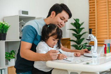 toddler girl scientist using tongs putting small herbal sample in slide with her father, preparing specimen for science microscope