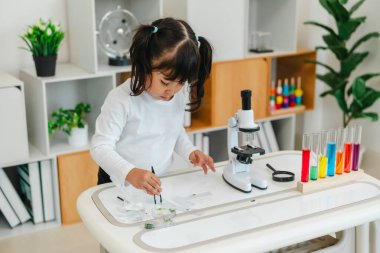 toddler girl scientist using tongs putting small herbal sample in slide, preparing specimen for science microscope