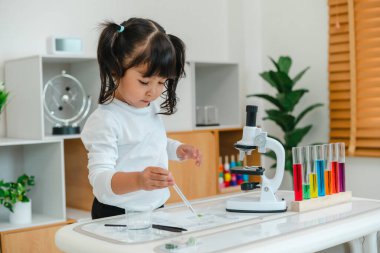 toddler girl scientist using pipette dropping of liquid being placed on a glass slide, preparing specimen for science microscope