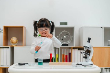 happy toddler girl scientist study using pipette dropping liquid with test tube and beaker. learning science
