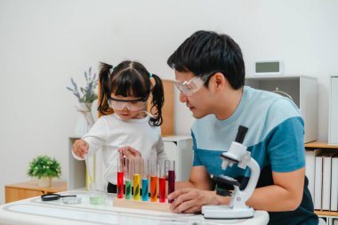 toddler girl scientist study using pipette dropping liquid with test tube and beaker. learning science with her father