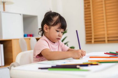 toddler baby girl training to drawing with colored pencil on a desk at home
