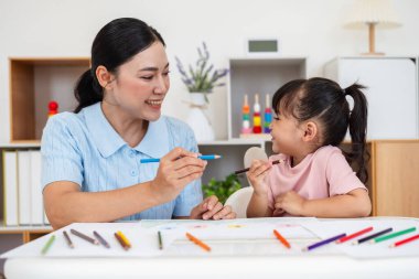 toddler baby girl training to drawing with colored pencil with mother helping on a desk at home