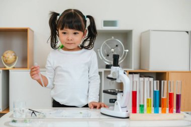 happy toddler girl scientist using pipette dropping of liquid being placed on a glass slide, preparing specimen for science microscope