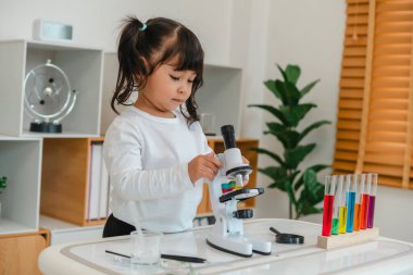 Küçük kız bilim adamı mikroskopla bilim öğreniyor.