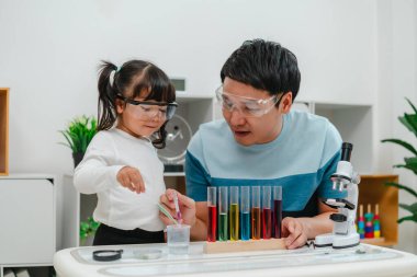 toddler girl scientist study using pipette dropping liquid with test tube and beaker. learning science with her father