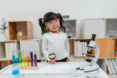 happy toddler girl scientist is holding a magnifying glass and learning about science