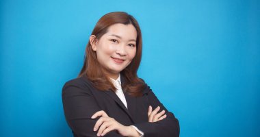 Kollarını kavuşturup mavi arka planda duran Asyalı iş kadını kameraya poz verdi