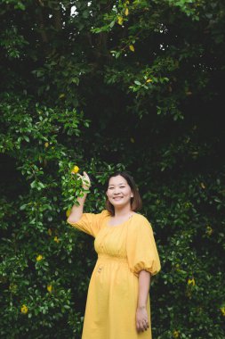 Yaprak doğa duvarında sarı elbisesi olan mutlu hamile Asyalı kadın.